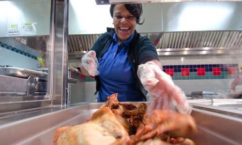 Cafeteria worker loading roast chicken onto serving trays